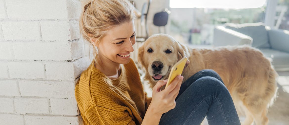 Frau mit Hund schaut lachend aufs Handy
